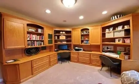 A "before" perspective of a large kitchen in Geist showing the initial stage of painting old kitchen cabinets before a complete color change. The image highlights a expansive, multi-angled kitchen island with light-colored countertops and decorative corbels, all finished in a solid gray tone. The surrounding cabinetry, which includes both solid and glass-front doors, is also painted gray to match, set against rich hardwood flooring and a modern stainless steel refrigerator. This baseline photo documents the kitchen's status during the professional refinishing process managed by the guy painting team.