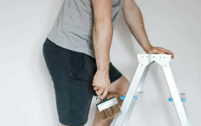 Painter on a step ladder cutting in a sharp line along the ceiling and trim.