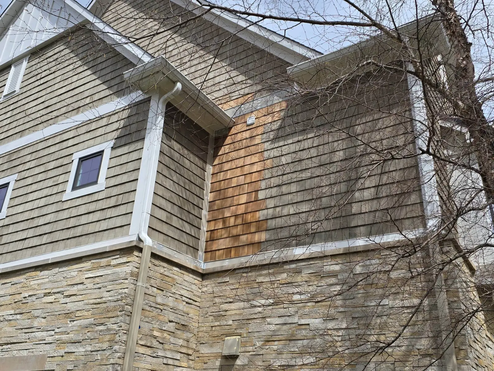 A high-angle view of a residential home's exterior showing a freshly repaired section of cedar shingle siding. This precise wood replacement and integration is a key component of our exterior painting indianapolis services in geist. Guy painting ensures that all damaged natural wood elements are restored to original standards before applying protective coatings to preserve the home's aesthetic and structural integrity.